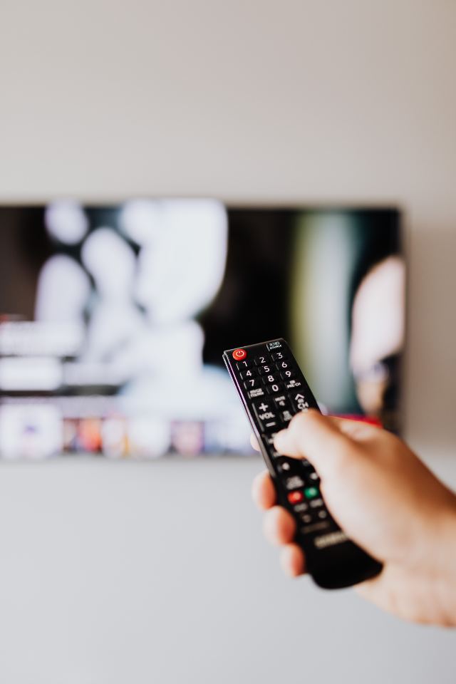 Mão apontando o controle remoto para a televisão